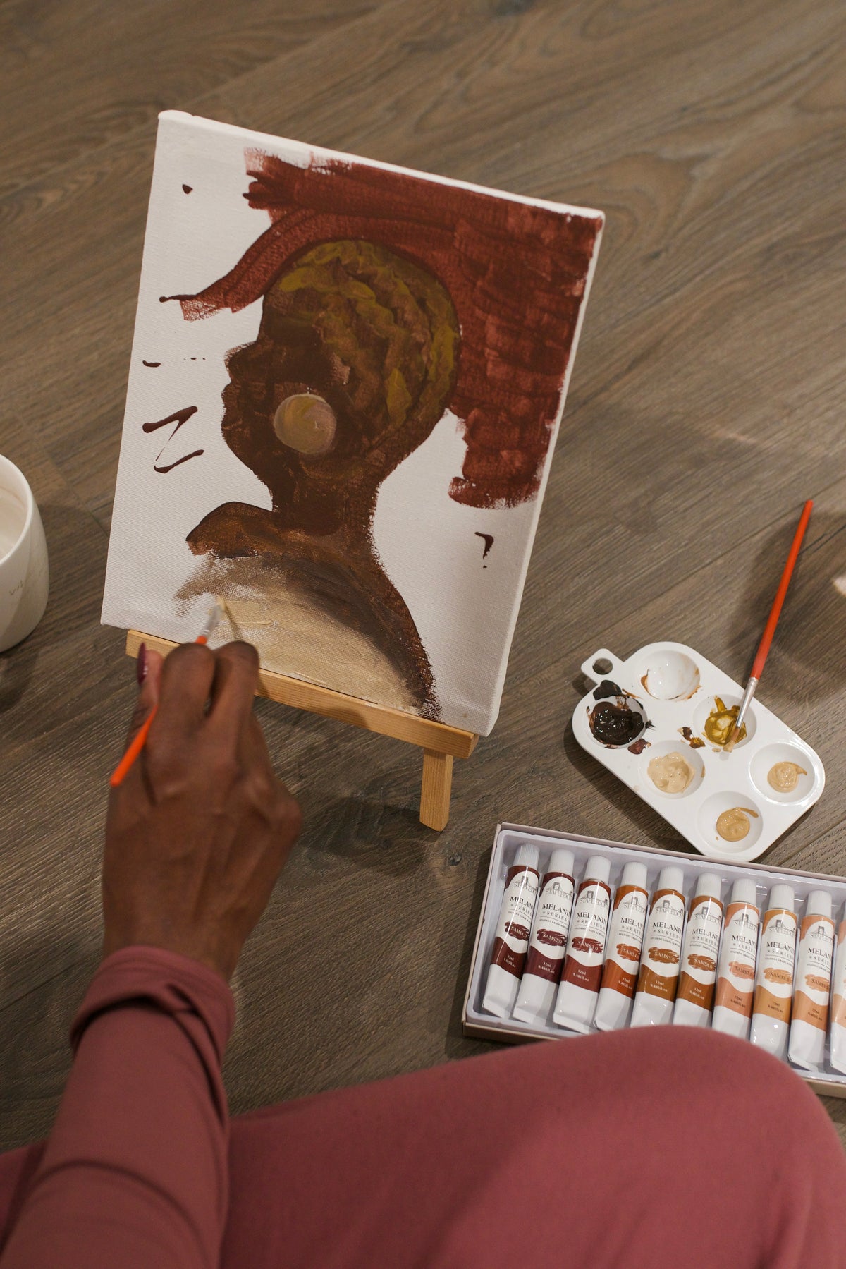 person painting a portrait on a white canvas with shades of brown acrylic paints