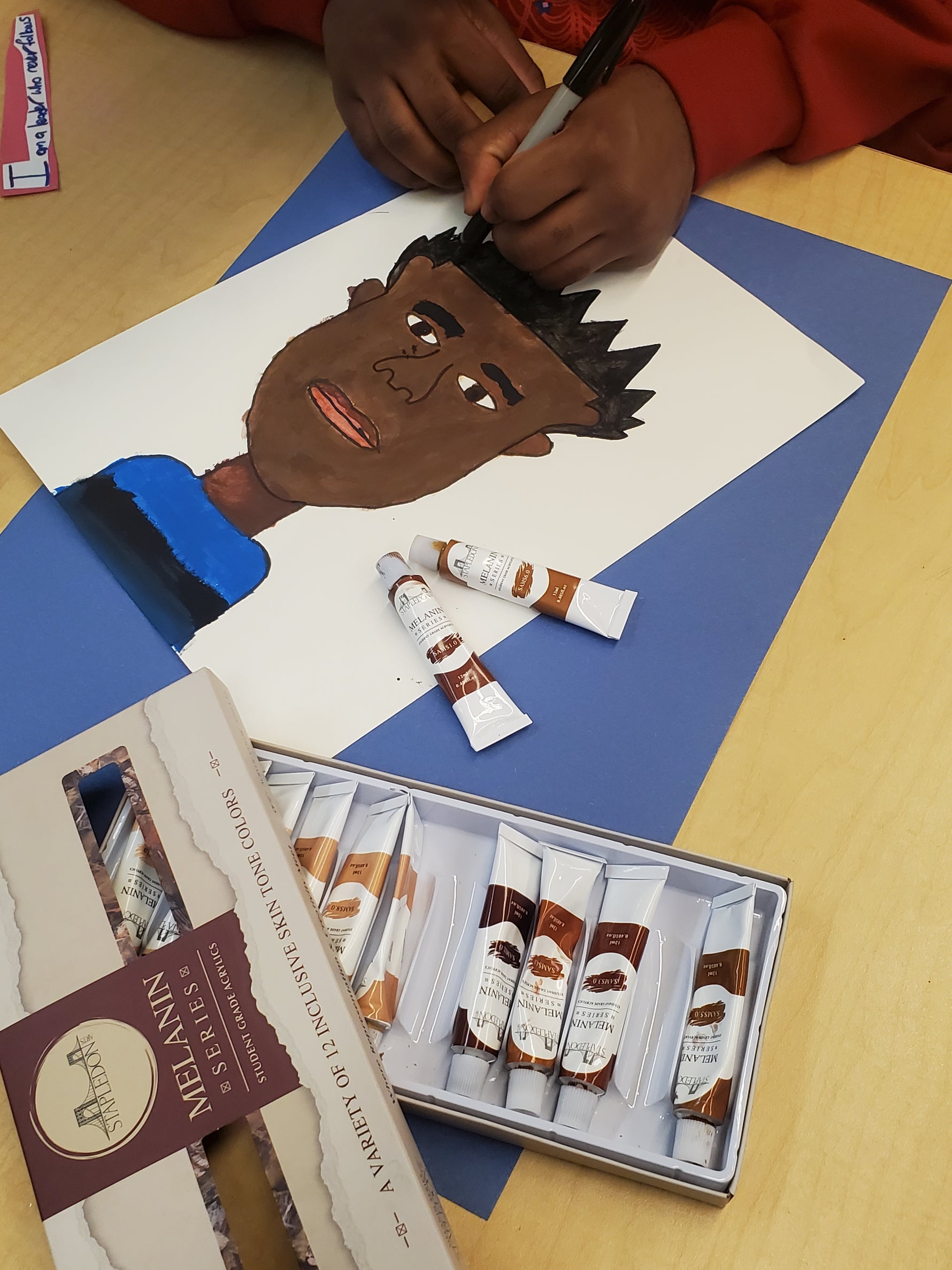 student creating a self portrait using melanin toned paints and markers