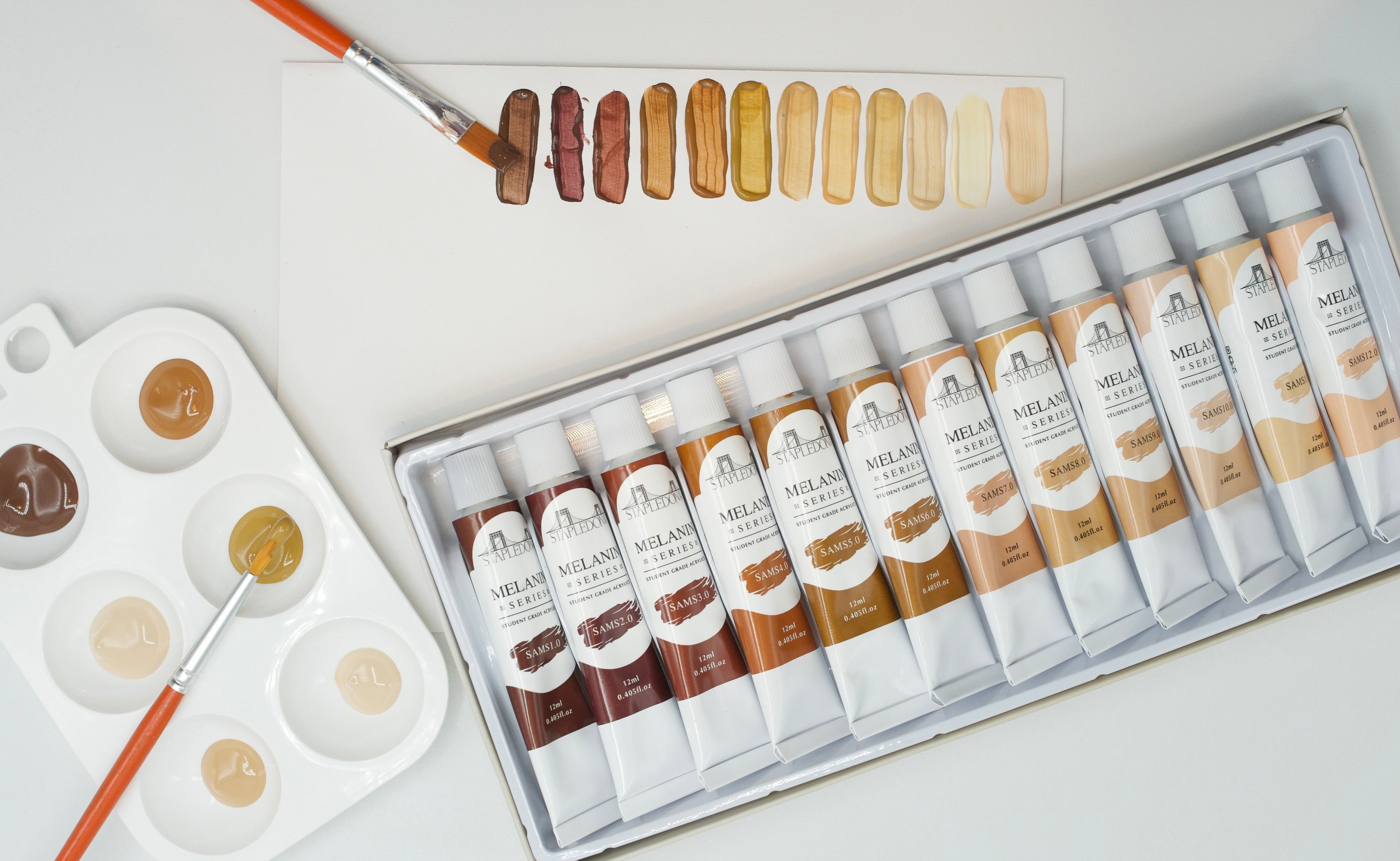 Artists table with skin tone acrylic paints, freshly painted swatches, and a palette of paints.