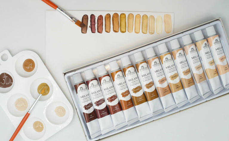 Artists table with skin tone acrylic paints, freshly painted swatches, and a palette of paints.